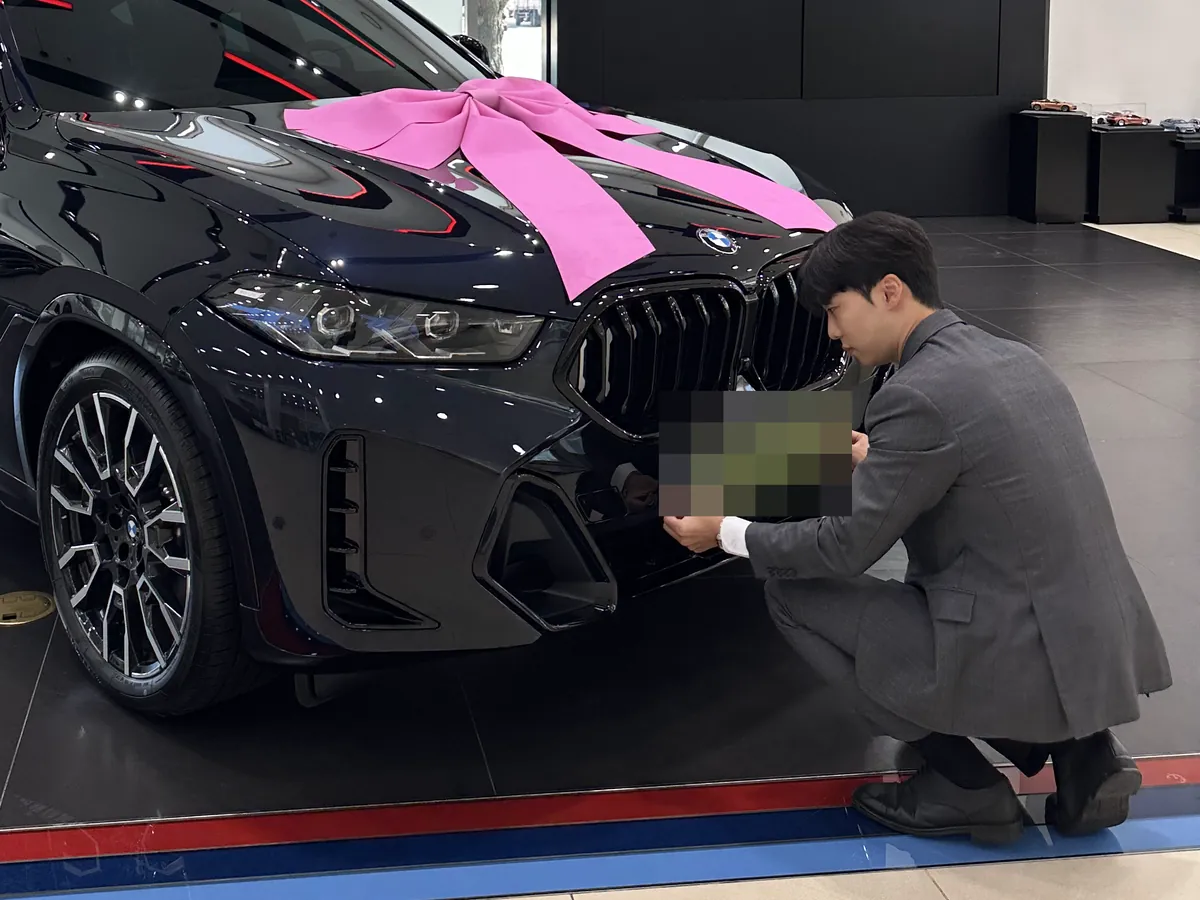 우상남이 분홍 리본을 단 검은 BMW X6 앞 번호판을 다는 모습 — 번호판은 가림